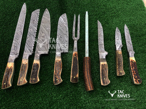 A set of eight custom knives and a carving fork with Damascus steel blades and natural antler handles, arranged on a green artificial turf background. The Tac Knives logo is visible on the image.