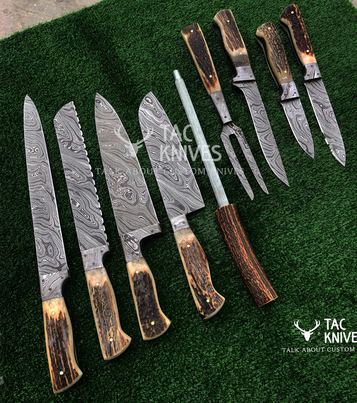 A set of custom knives and a carving fork with patterned Damascus steel blades and natural brown antler handles, arranged on a green textured background. The Tac Knives logo is visible on the blades and as a watermark.