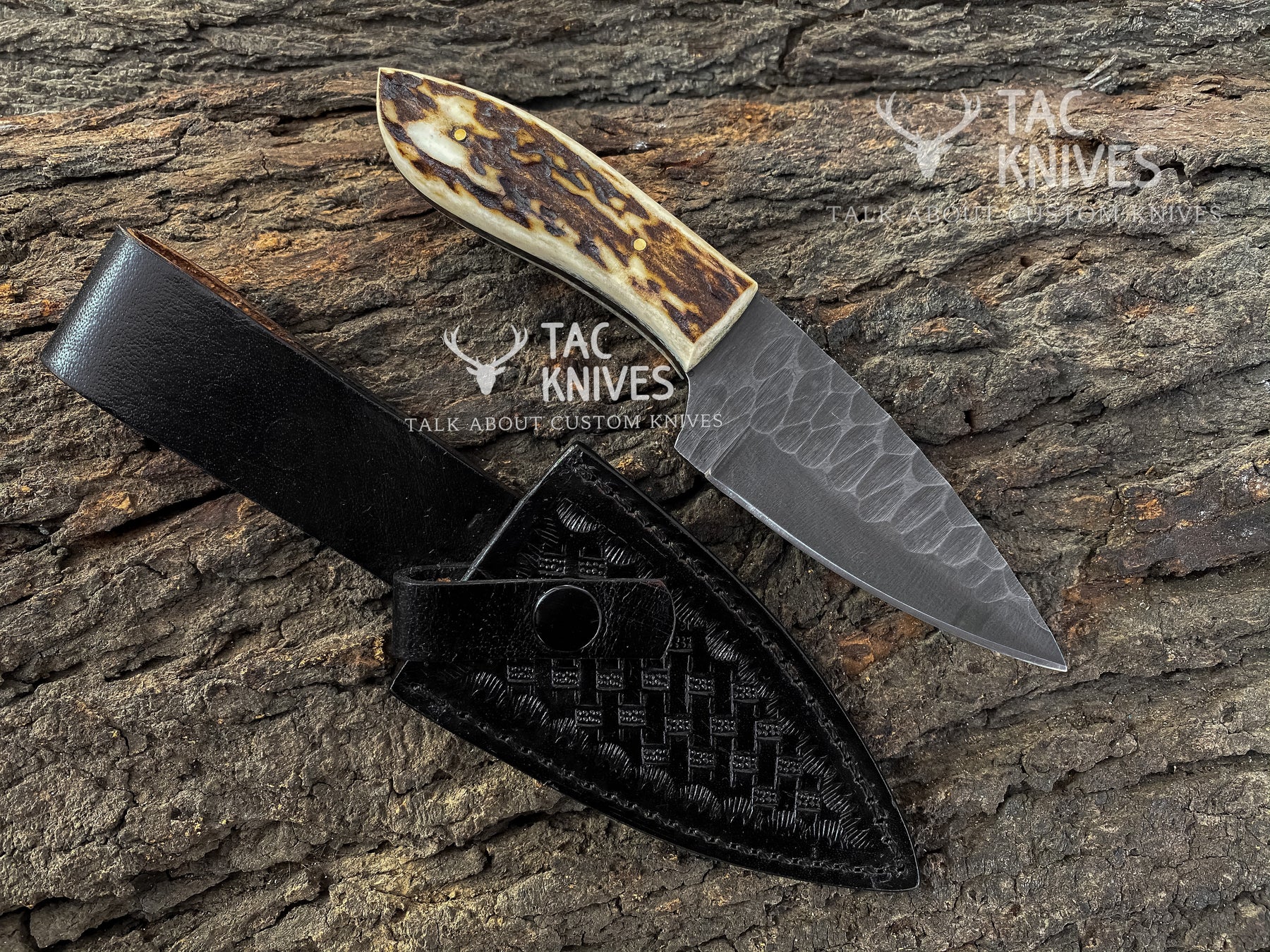 A custom fixed-blade knife with a textured gray steel blade and a carved bone handle, displayed next to its black woven leather sheath on a textured tree bark background. Watermarks for 'TAC KNIVES' are visible on the image.