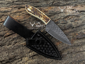 A custom fixed-blade knife with a textured gray steel blade and a carved bone handle, displayed next to its black woven leather sheath on a textured tree bark background. Watermarks for 'TAC KNIVES' are visible on the image.