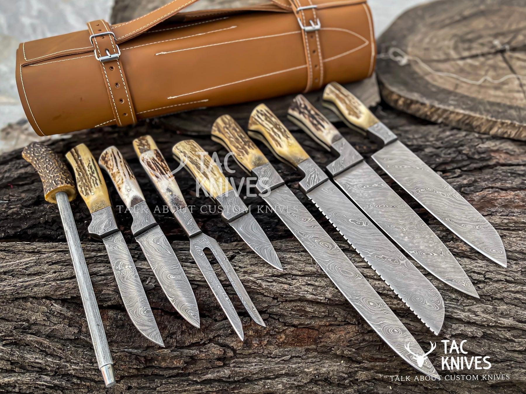 A set of custom hunting knives with patterned steel blades and natural antler handles, displayed on a rustic wood surface alongside a brown leather roll and a wood slice. The Tac Knives logo is visible.
