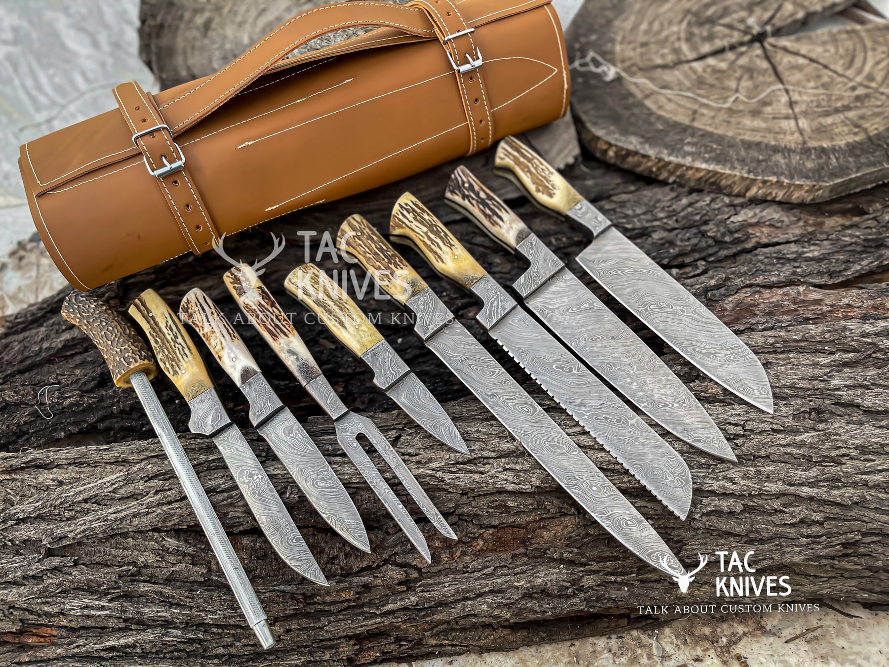 A set of custom hunting knives with patterned Damascus steel blades and antler-style handles, displayed next to a brown leather roll on a rustic wood background. The Tac Knives logo is visible in the bottom right corner.